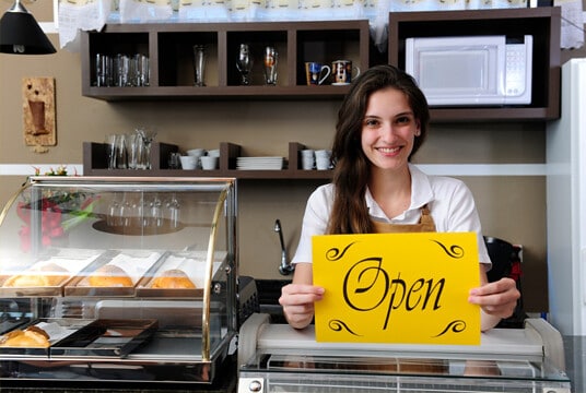 Store owner holding open sign thanks to small business grants